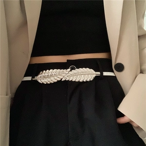 Detail of silver leaf buckle and slim white elastic waist belt on black trousers