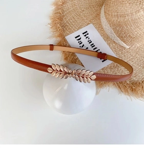Detail of leaf-shaped gold buckle on elegant brown leather belt for women outfit