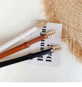 Detail of leaf-shaped metal buckles on three slim PU leather belts in white, brown, and black