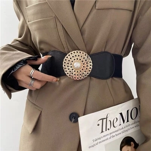 Détail de la ceinture élastique noire avec boucle ronde dorée et perle sur un costume kaki