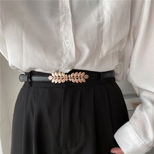 Elegant thin black leather belt for women with decorative gold leaf buckle on white shirt