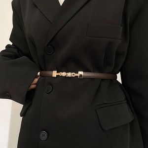 Dettaglio di una sottile cintura in pelle marrone con fibbia dorata e perle su abito nero