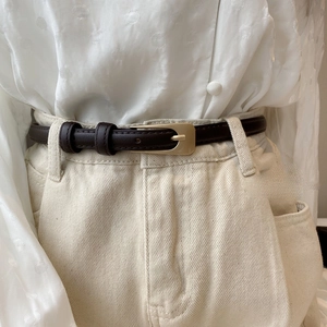 Detailed view of dark brown PU leather thin belt styled on cream denim pants with gold buckle