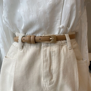 Close-up of slim khaki leather belt with matte gold buckle on white polka dot shirt