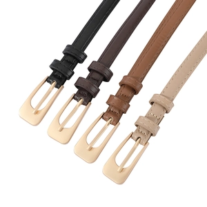 Close-up of four slim PU leather belts in black and brown with gold buckles