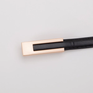 Détail d'une ceinture fine en cuir noir avec une boucle rectangulaire en or rose