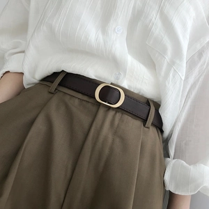 Ceinture femme minimaliste marron foncé avec boucle dorée ovale sur un pantalon