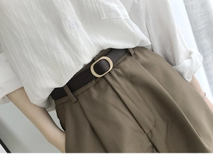 Détail d'une ceinture fine en cuir marron foncé avec boucle ovale dorée élégante