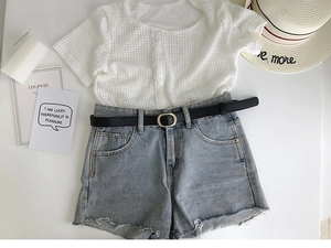 Détail d'une fine ceinture noire avec un short en jean effiloché et un haut blanc gaufré