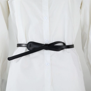 Detailed view of a slim black PU leather belt tied in a bow over a white shirt