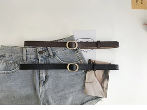 Détail de fines ceintures noires et marron avec boucles dorées sur short en jean