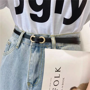 Close-up of a slim black PU leather belt with a gold double ring buckle on blue jeans