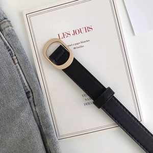 Détail d'une ceinture en cuir noir avec boucle dorée ovale sur un jean en denim bleu