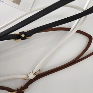 Close-up of thin PU leather belts in black, white, and brown with gold oval buckles