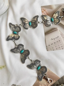 Close-up of butterfly metal chain belt with inlaid turquoise stones on white fabric
