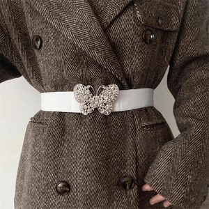 Détail d'une ceinture élastique blanche avec une grande boucle papillon ornée de strass
