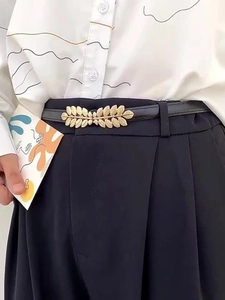 Detail of slim black belt with gold leaf buckle worn on black trousers and white shirt