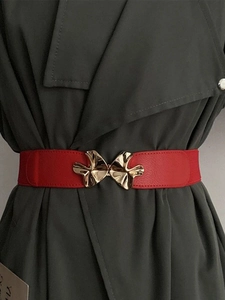 Detail view of red elastic waist belt with gold abstract mushroom buckle on coat
