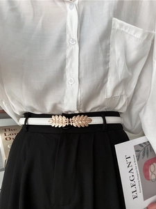 Detail of thin white belt with gold leaf buckle on black pants and white shirt