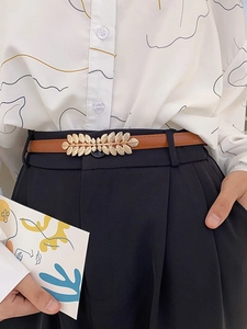 Detail of a thin brown leather belt with gold leaf buckle on white patterned blouse