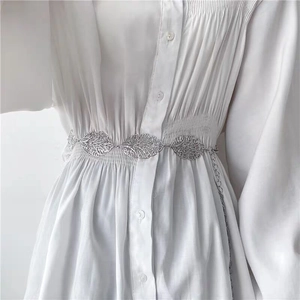 Detailed view of silver leaf-shaped metal chain belt paired with a white dress