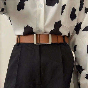 Minimalist brown leather belt with silver rectangular buckle on black trousers