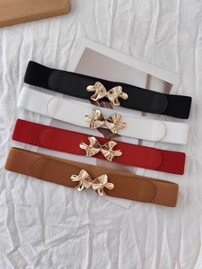 Detail of four colorful elastic waist belts with golden floral buckles on white fabric