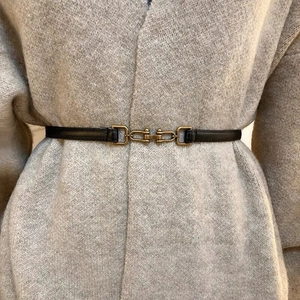 Detail of slim black leather belt with gold interlocking buckle on grey cardigan