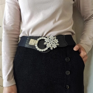 Detail of floral rhinestone buckle on black elastic belt with faux crocodile leather trim