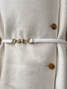 Close-up of a slim white leather belt with a gold metal buckle on a beige wool coat