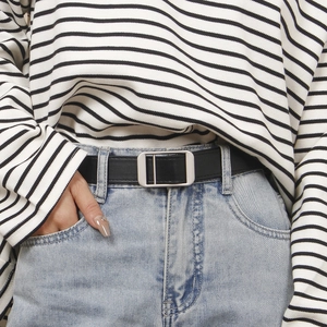 Detail view of a minimalist black leather belt with silver rectangular metal buckle on jeans