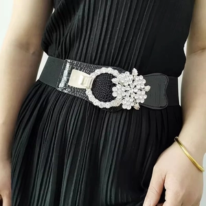 Close-up of black elastic belt featuring a flower-shaped silver buckle with sparkling rhinestones