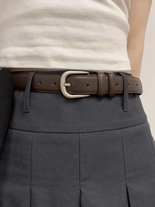 Close-up of minimalist dark brown leather belt with silver pin buckle on pleated skirt