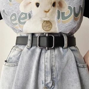 Detail shot of a slim black vintage leather belt with silver square metal buckle on jeans