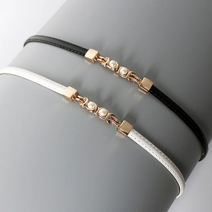 Close-up of black and white slim leather belts with gold metal links and pearls