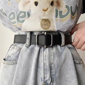 Close-up of black leather belt with gunmetal square buckle on blue jeans for men