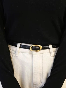 Détail d'une fine ceinture en cuir noir avec boucle métallique dorée moderne sur la taille