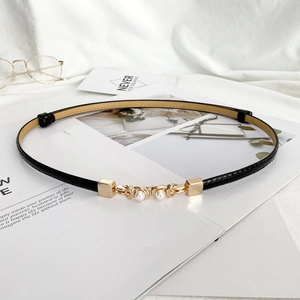 Gros plan sur une ceinture en cuir noir avec boucle dorée et perles sur tissu blanc