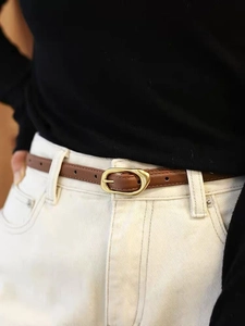 Gros plan d'une fine ceinture en cuir marron avec boucle dorée sur un jean blanc
