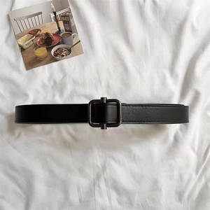 Flat lay of vintage black leather belt with a gunmetal square buckle on white fabric