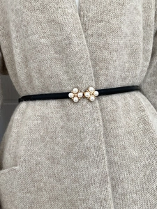 Detail of elegant black skinny belt featuring gold-tone flower buckles with pearl accents
