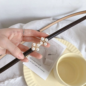 Detail of slim brown leather belt featuring elegant gold finish with inlaid pearls