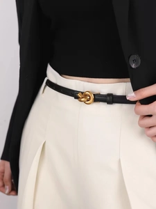 Detail of a thin black leather belt with a distinctive gold-tone knot buckle on white pants