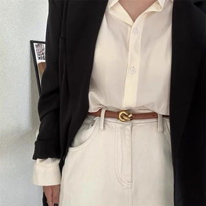 Close-up of thin brown leather belt with gold twist buckle on white jeans and black blazer