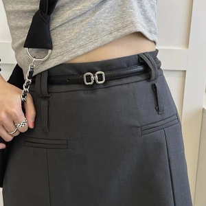 Detail of slim black PU belt with silver double square buckle on grey pleated skirt