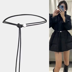 Détail d'une fine ceinture en corde noire nouée avec boucle ronde argentée