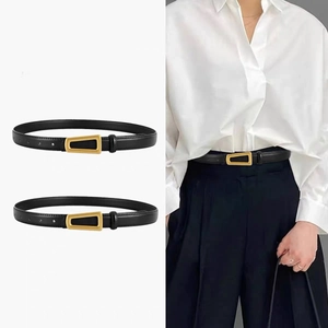 Détail de la fine ceinture en cuir noir avec une boucle en métal doré trapézoïdale