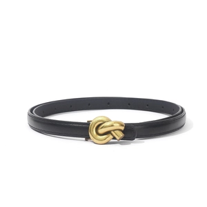 Detail of the golden metal knot buckle on a black slim leather belt for women