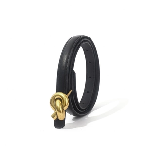 Detailed macro view of the vintage gold knot buckle on a slim black leather belt