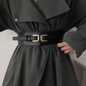 Dettaglio cintura nera elastica alta con doppie fibbie dorate su un trench grigio